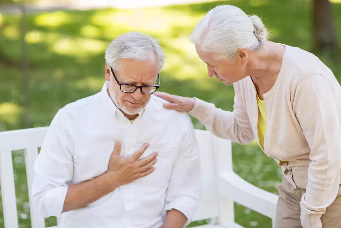 Image of a man sitting down grabbing his chest while a woman comforts him