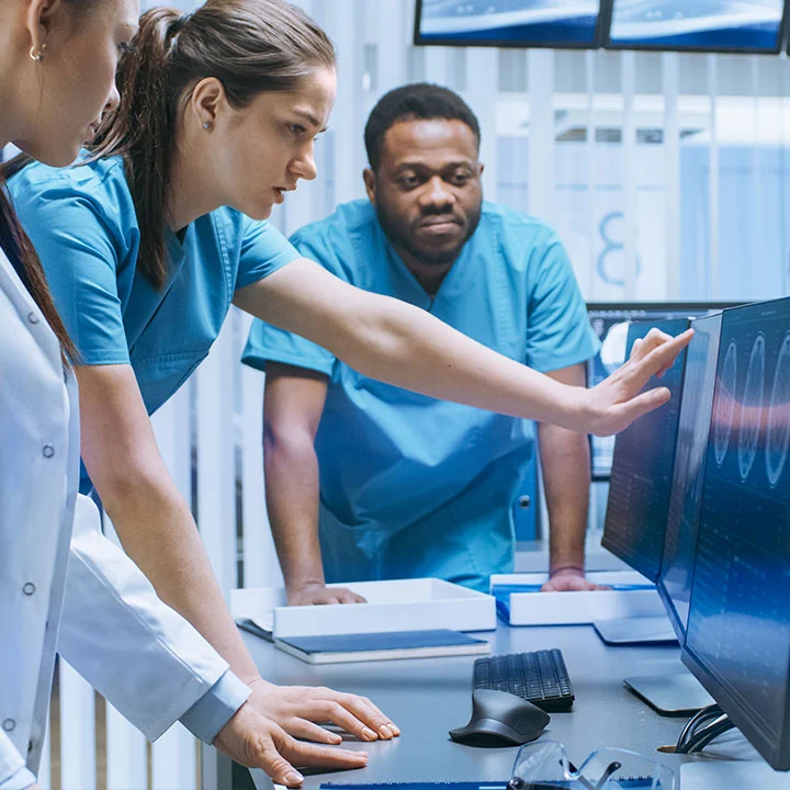 Image of three people in scrubs looking at a computer screen with a blue hash pattern overlay